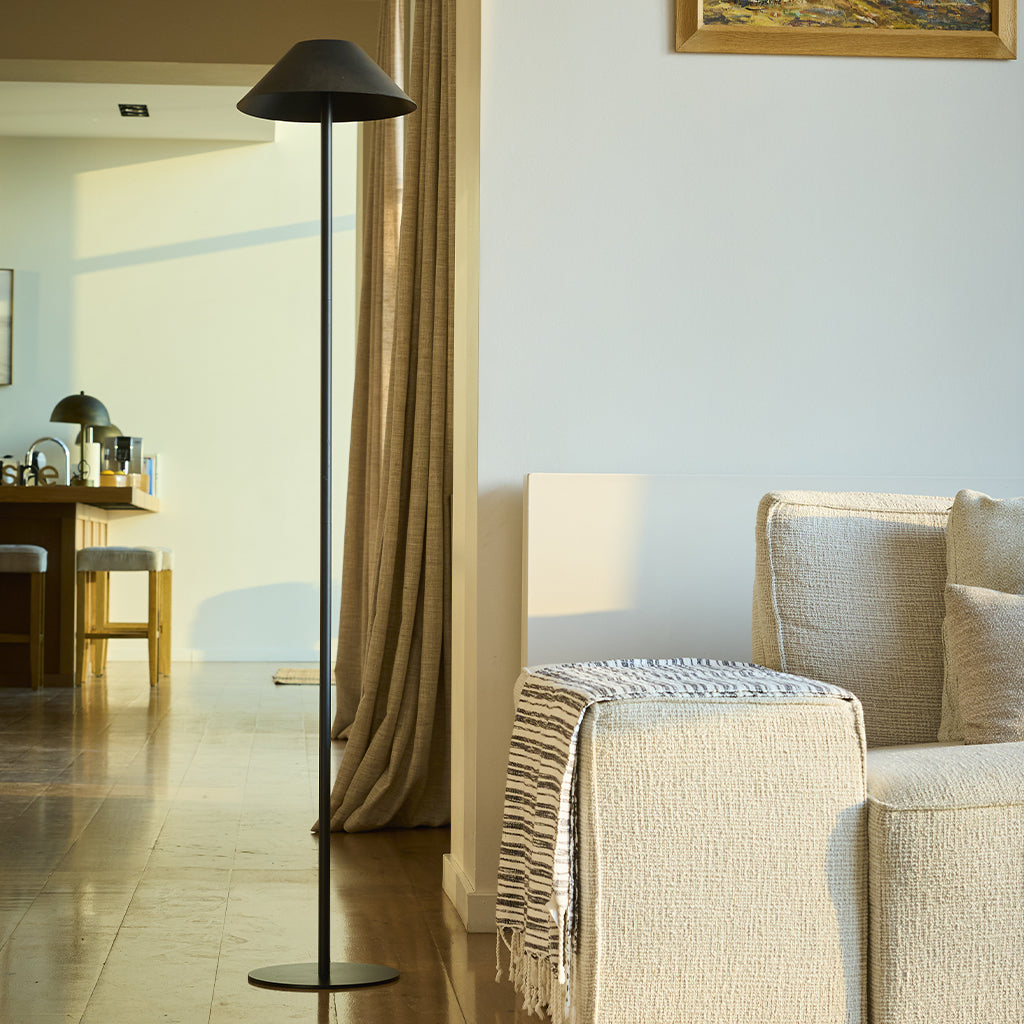 Ein modernes Wohnzimmer mit Stehlampe, Couch und Blick in einen anderen Raum mit Tisch und Stühlen.