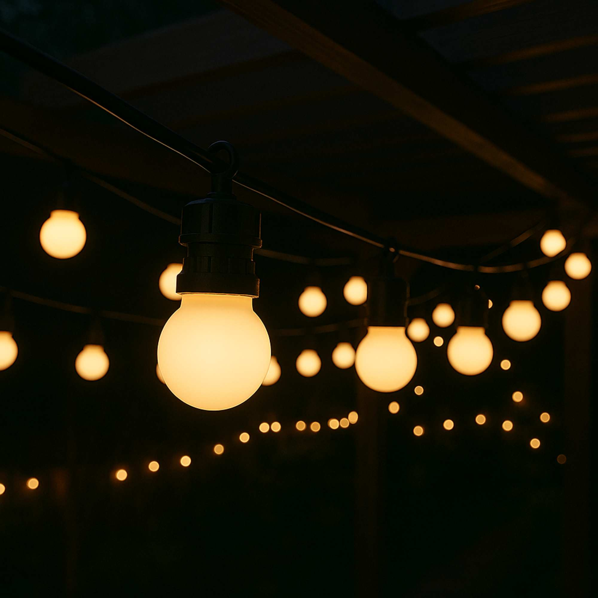 Luces de cadena con bombillas brillantes cuelgan contra un fondo oscuro. Las luces son cálidas, creando un ambiente acogedor.