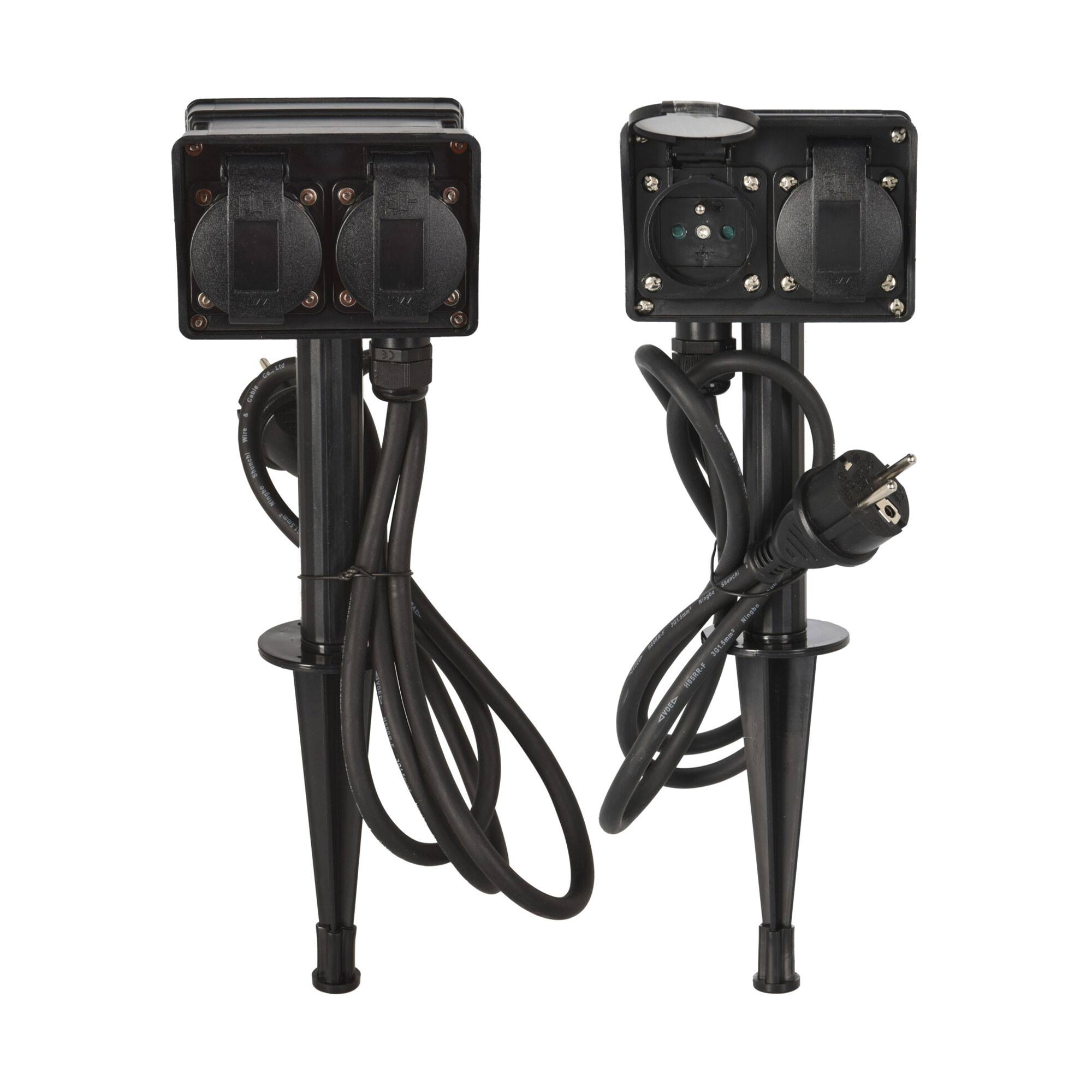 Dos enchufes negros para exteriores sobre estacas con cables y enchufes negros, sobre un fondo blanco.