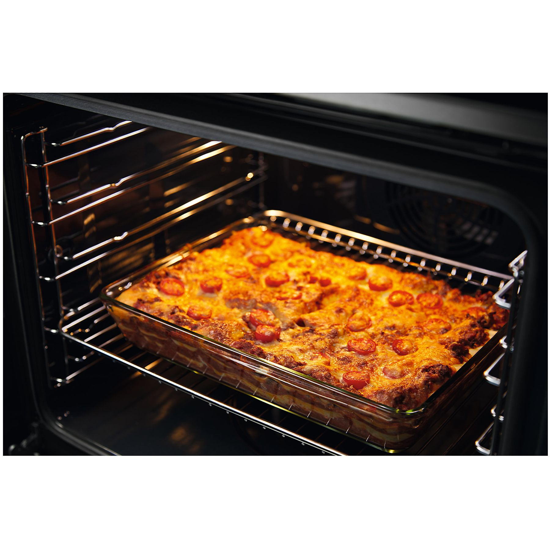 Lasagna in forno. Il piatto ha formaggio e pomodori sopra. L'interno del forno è nero con griglie metalliche.