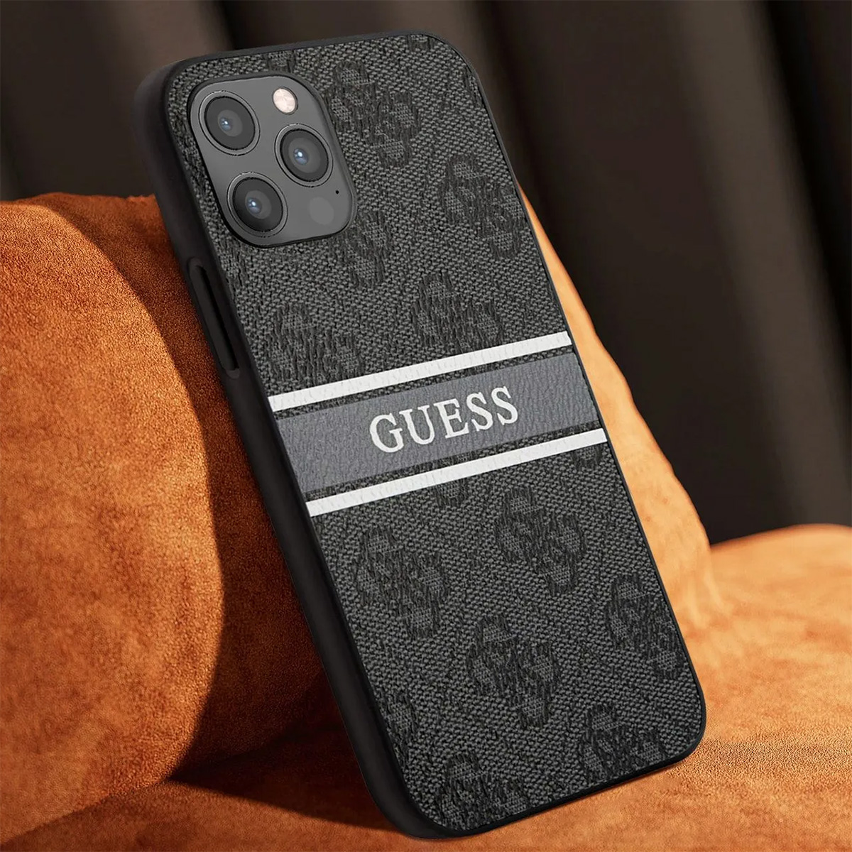 Una custodia per telefono con logo Guess. La custodia è nera con un motivo strutturato. Il telefono poggia su una superficie arancione.