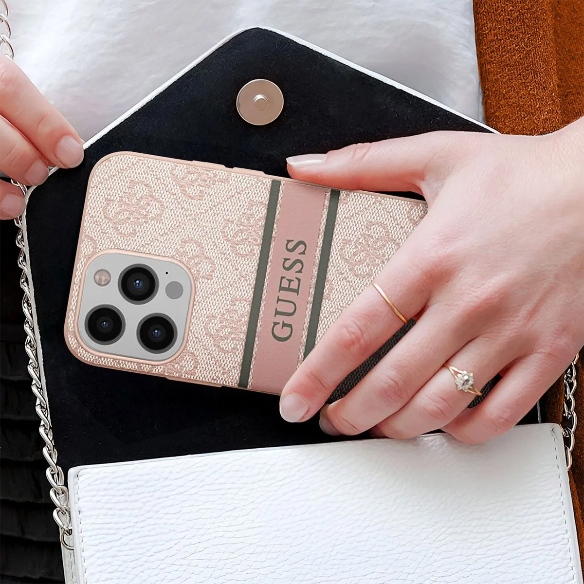 Una donna tiene una custodia per telefono Guess in una borsa. La custodia è rosa con logo, anello d'oro e anello di diamanti.