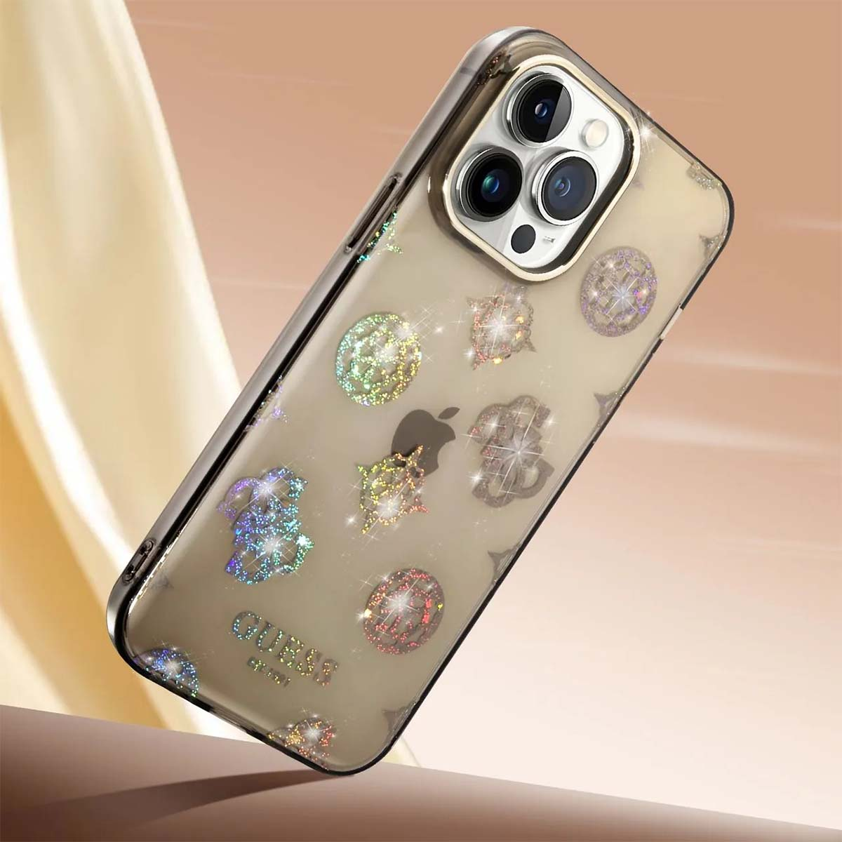 Una custodia trasparente per iPhone con dettagli dorati. Decorata con loghi e disegni scintillanti. Logo Guess in basso.