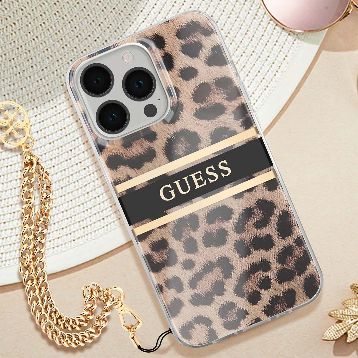 Una custodia per telefono con stampa leopardata e la scritta "GUESS". Catena d'oro, cappello e occhiali da sole sono visibili.