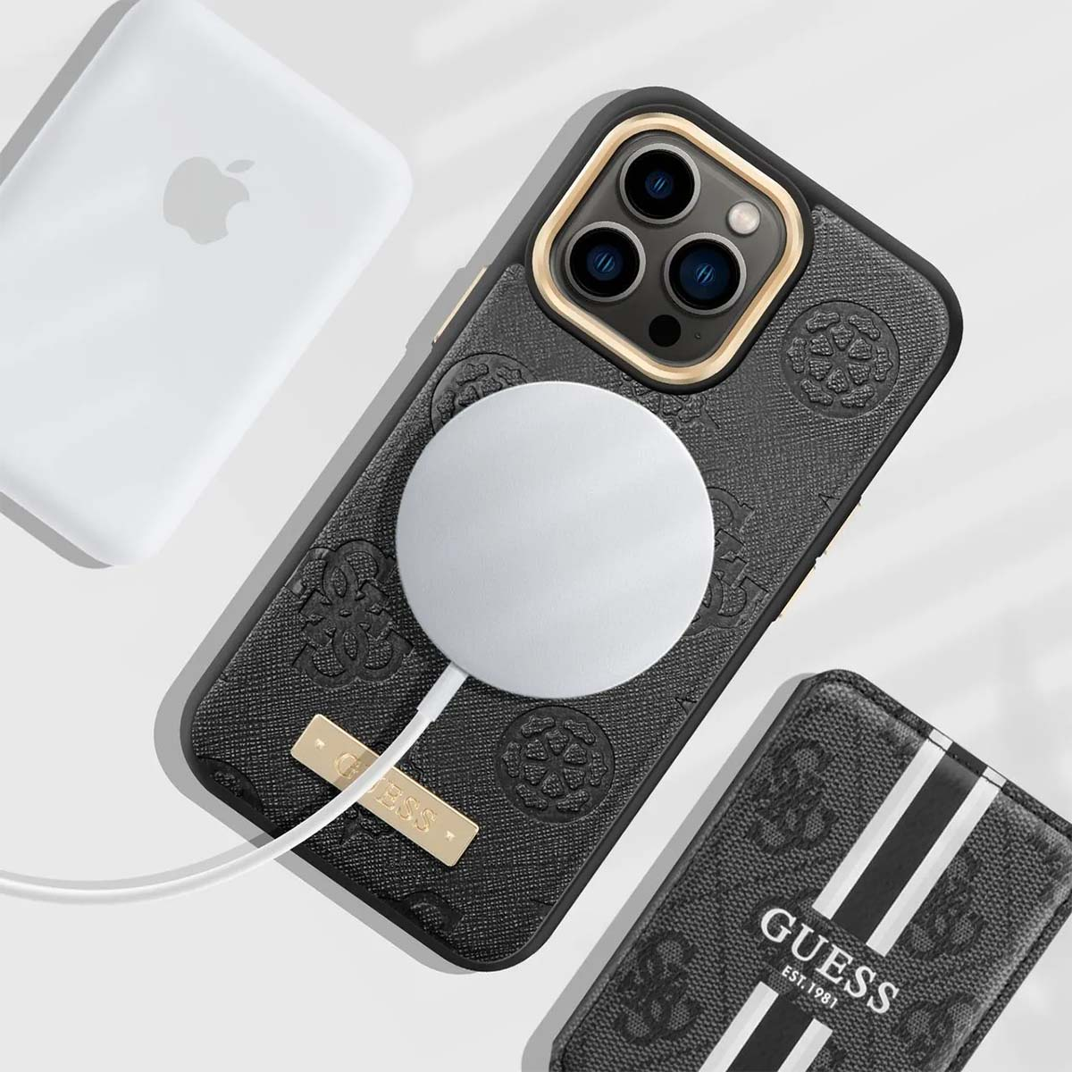 Custodia nera con logo Guess, caricatore bianco, caricatore Apple e portafoglio Guess su superficie bianca.