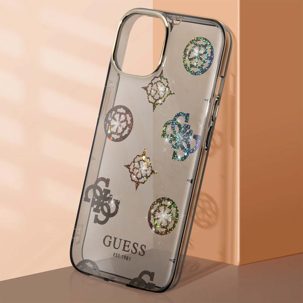 Una custodia Guess trasparente con loghi glitterati. La custodia è su una superficie riflettente, e lo sfondo è color pesca.