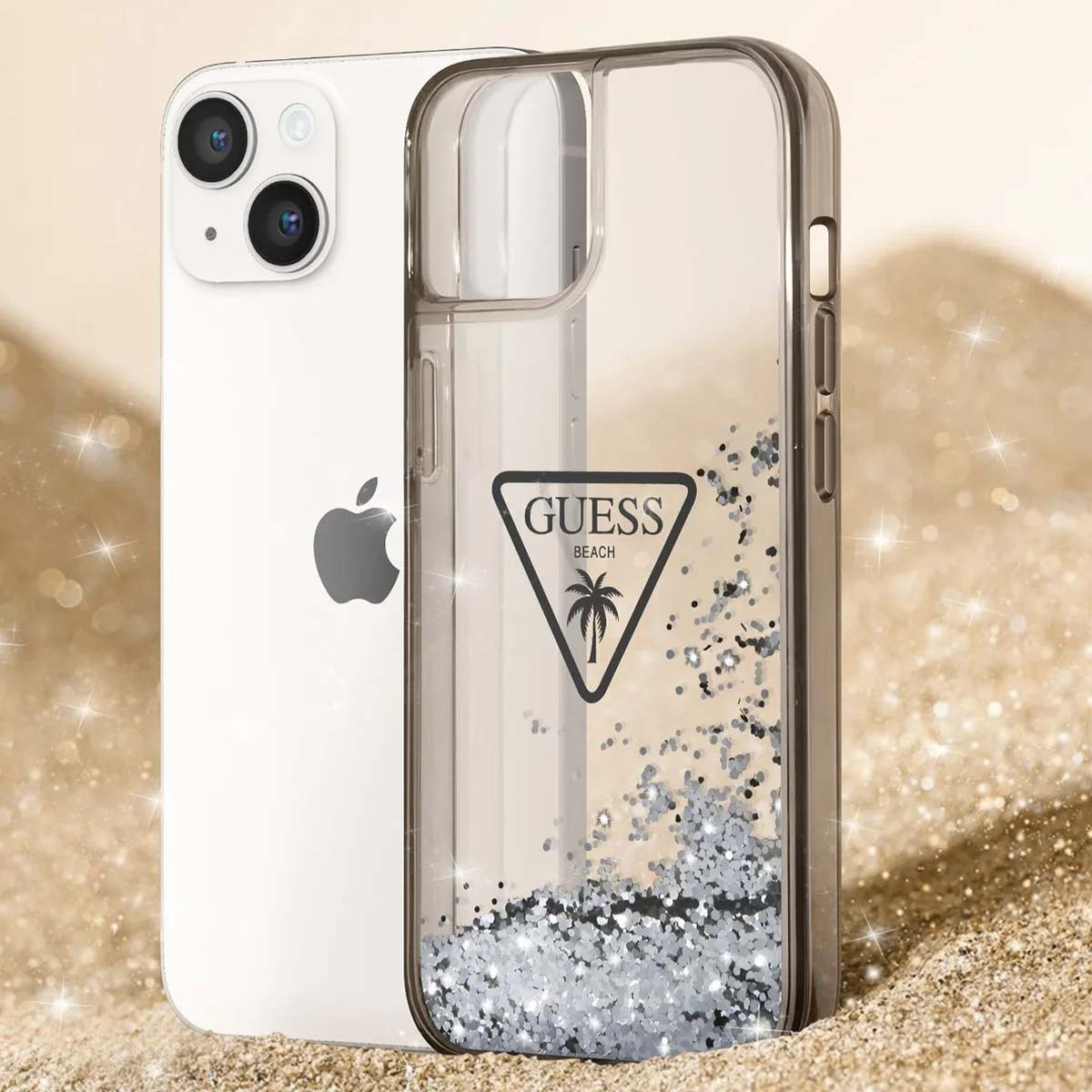 Un iPhone con custodia Guess Beach. La custodia trasparente ha glitter argentati e un logo Guess. Il telefono è sulla sabbia con riflessi scintillanti.