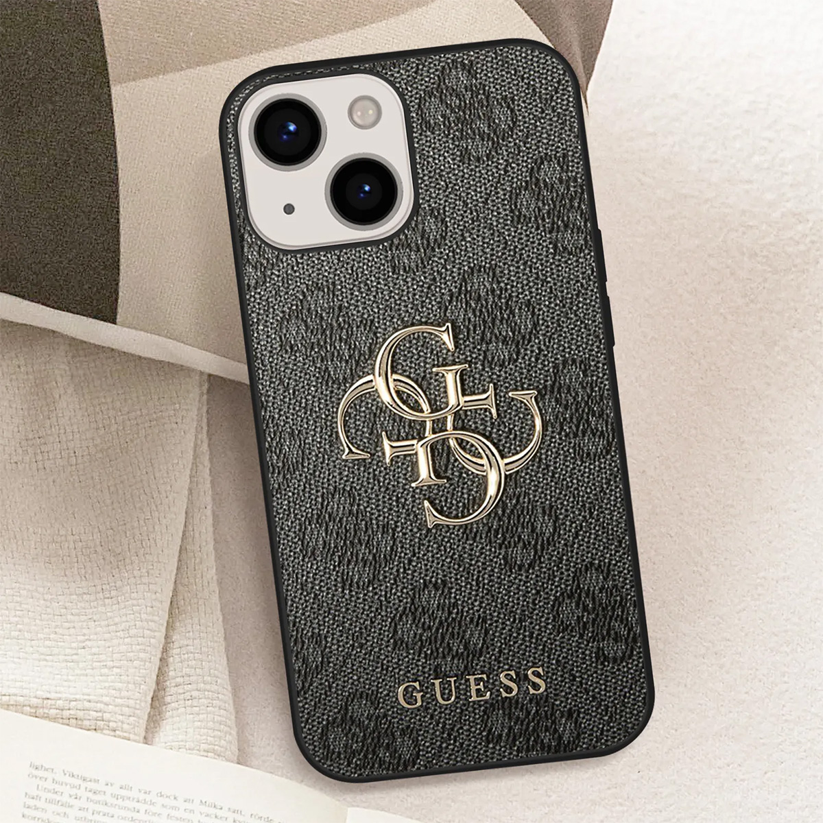 Primo piano di una custodia per telefono Guess. Custodia nera strutturata con logo e scritta dorati. Fotocamera del telefono visibile.