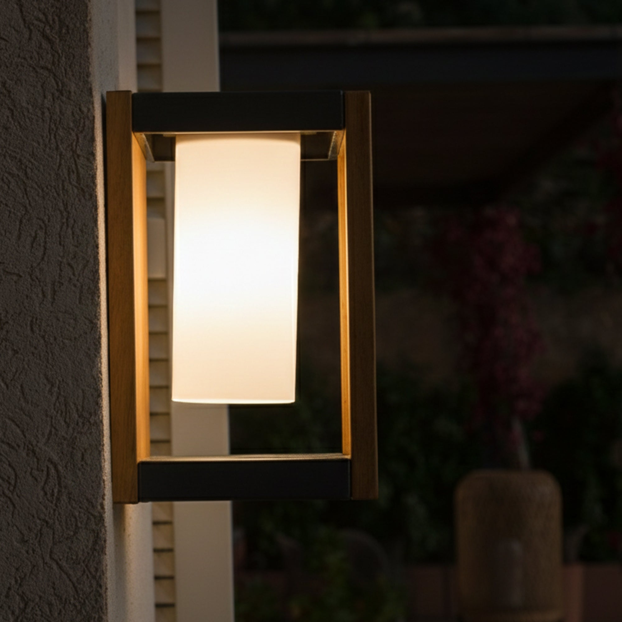 Eine rechteckige Außenlampe mit leuchtend weißem Mittelteil ist an einer strukturierten Wand befestigt. Der Hintergrund ist verschwommen.