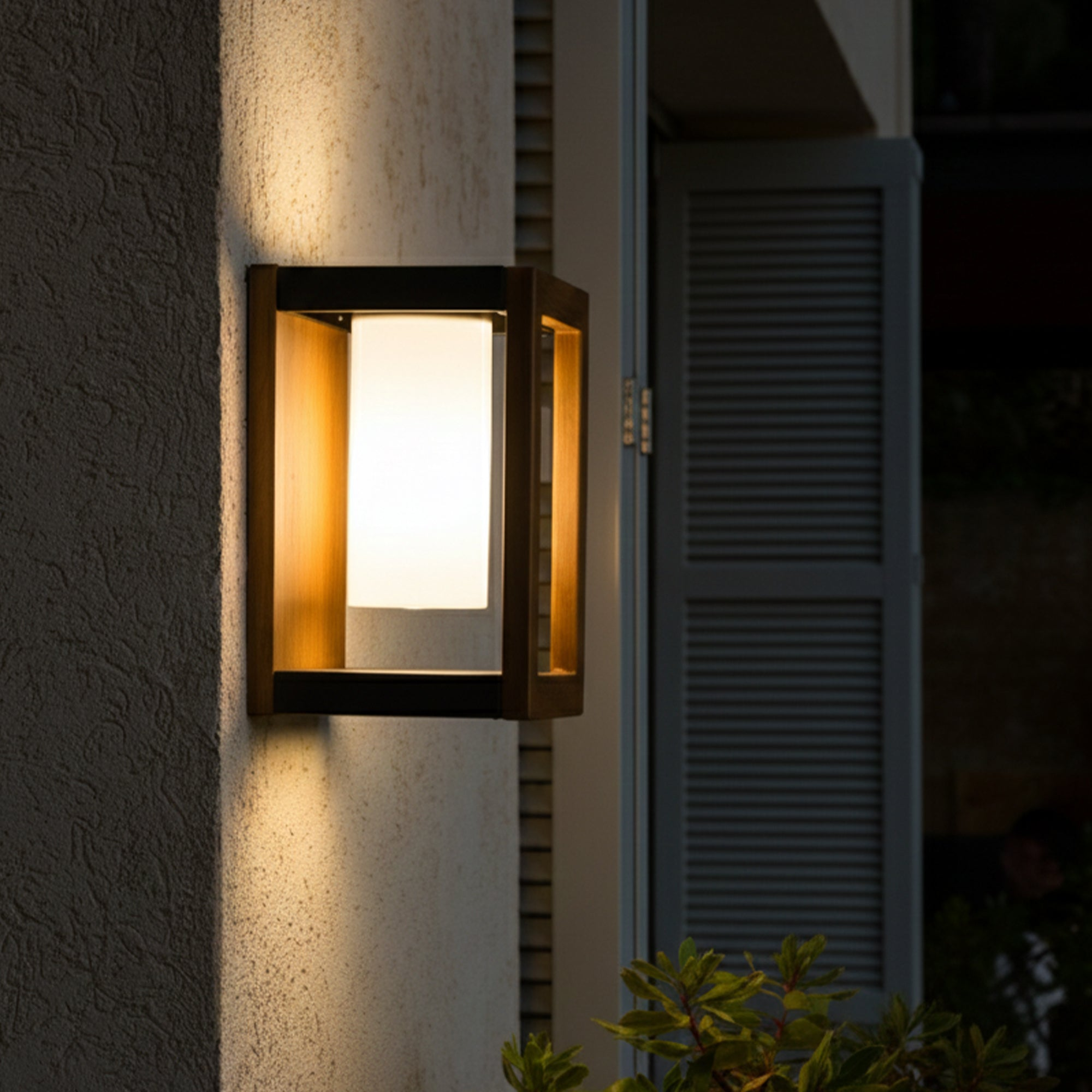 Eine beleuchtete Wandlampe mit rechteckigem Holzrahmen ist an einer strukturierten Wand befestigt. Im Hintergrund befindet sich ein Fenster mit Fensterläden.