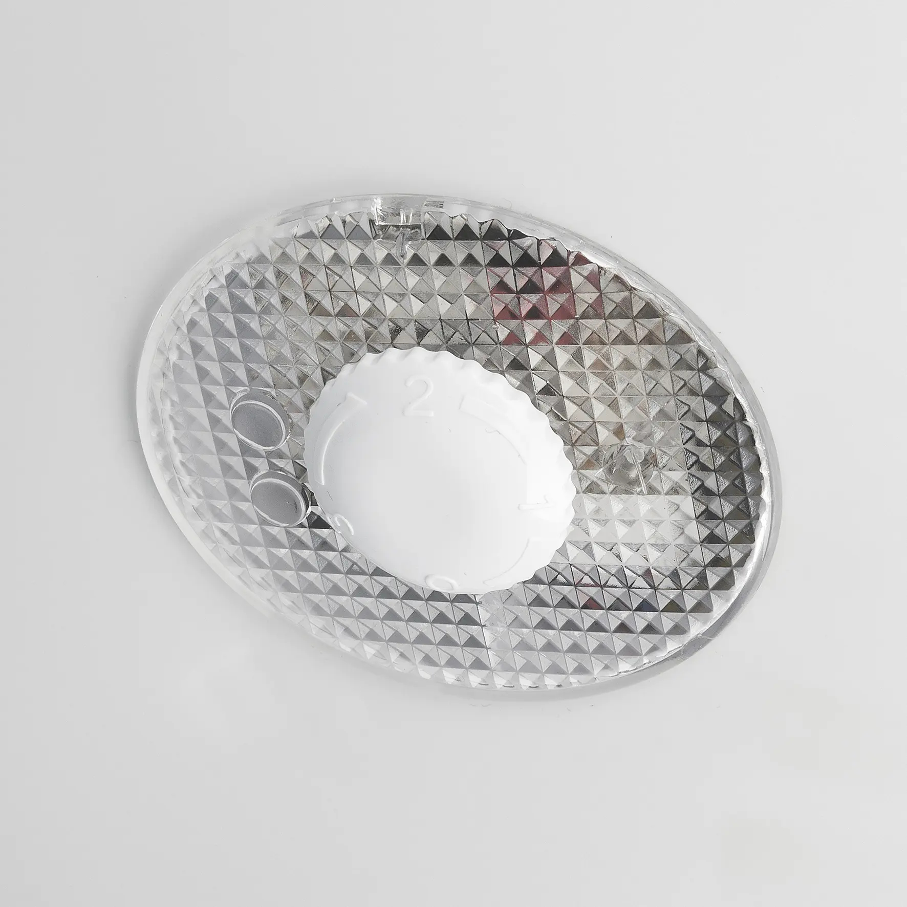 Primo piano di una manopola di controllo bianca su un pannello ovale di plastica trasparente con motivo a diamante, su sfondo bianco.