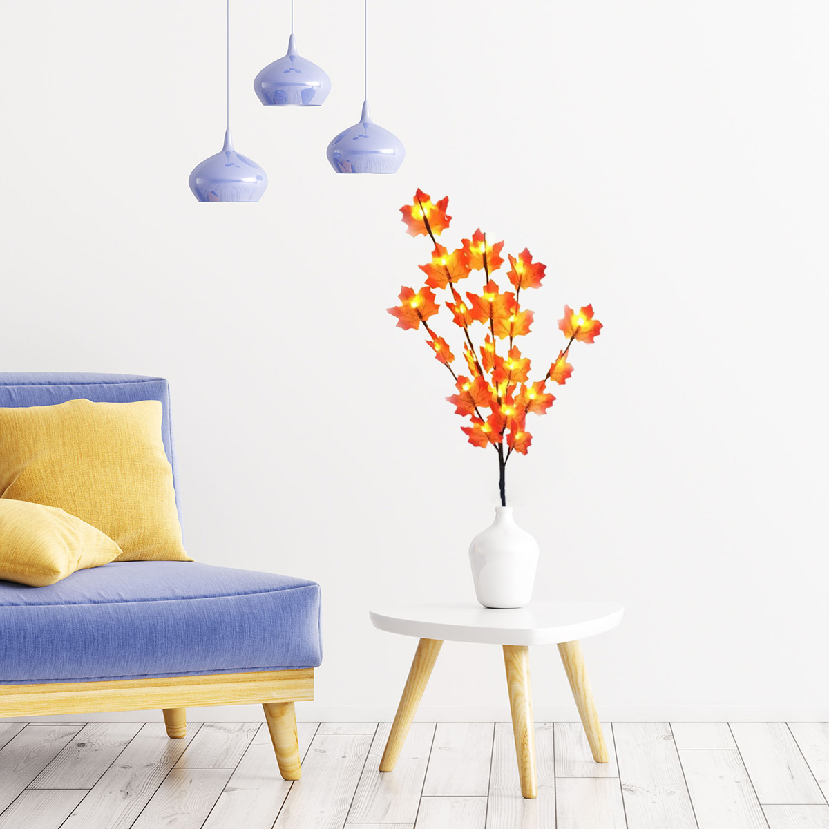 Blaues Sofa mit gelben Kissen, weißer Tisch mit Vase mit orangenen Blättern, drei blaue Pendelleuchten an weißer Wand.