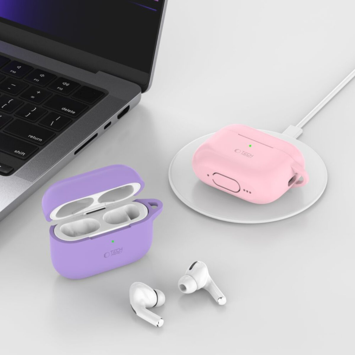 Image shows AirPods and cases. One purple case open, one pink case charging, and two AirPods. Laptop in background.