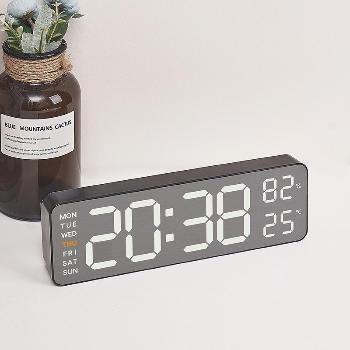 Eine Digitaluhr zeigt 20:38 an, mit 82 % Luftfeuchtigkeit und 25 Grad Celsius. Hinter der Uhr steht eine Vase mit Blumen.