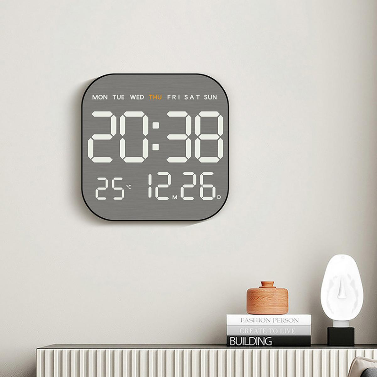 Eine Digitaluhr zeigt 20:38, Datum 12.26 und Temperatur 25°C an. Darunter Bücher und Dekoration auf einer schwarzen Oberfläche.