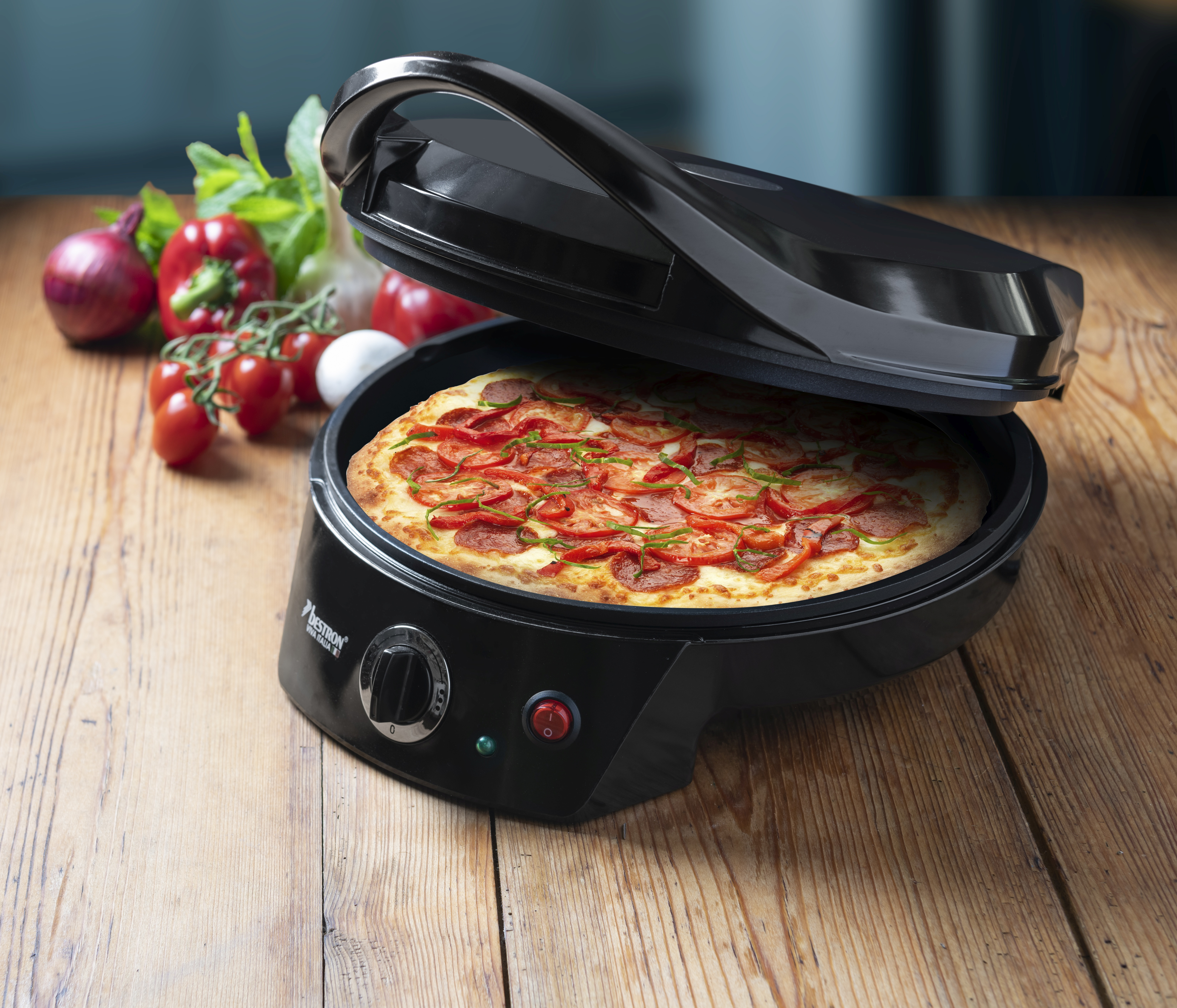 Una pizza in un'apparecchiatura per pizza nera con verdure su un tavolo di legno.