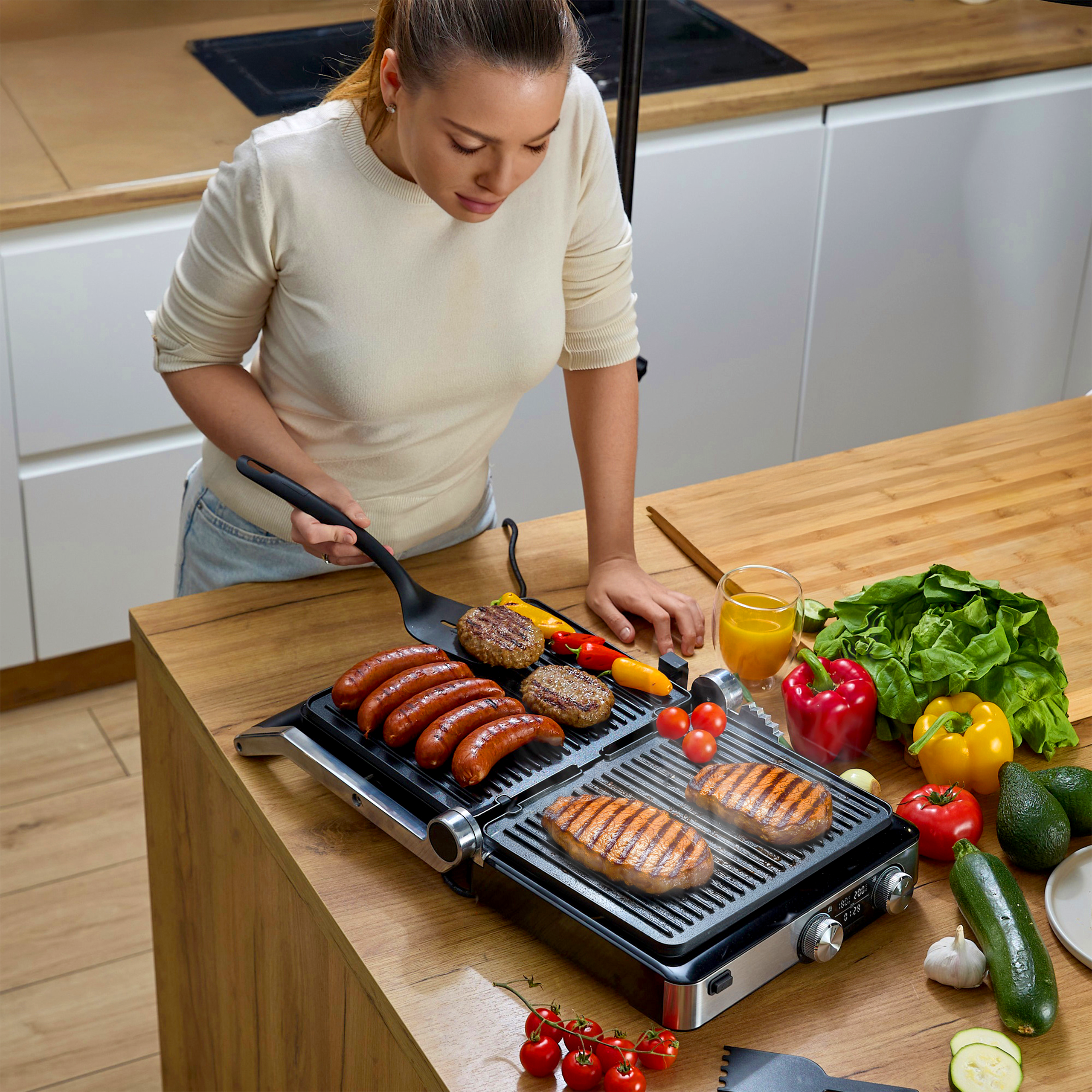 Kobieta grilluje jedzenie na grillu elektrycznym. Warzywa i sok na blacie. Kobieta trzyma szpatułkę.