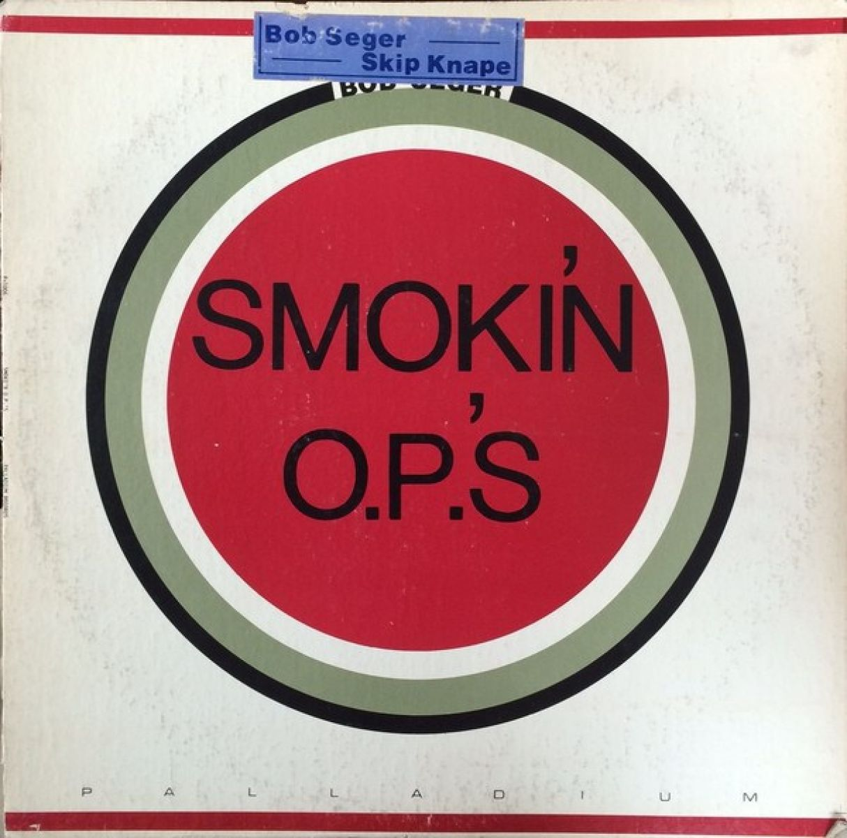 Albumhoes voor Bob Seger's 'Smokin' O.P.'s'. Toont een rode cirkel met zwarte tekst, omringd door groene en zwarte ringen, op een witte achtergrond.