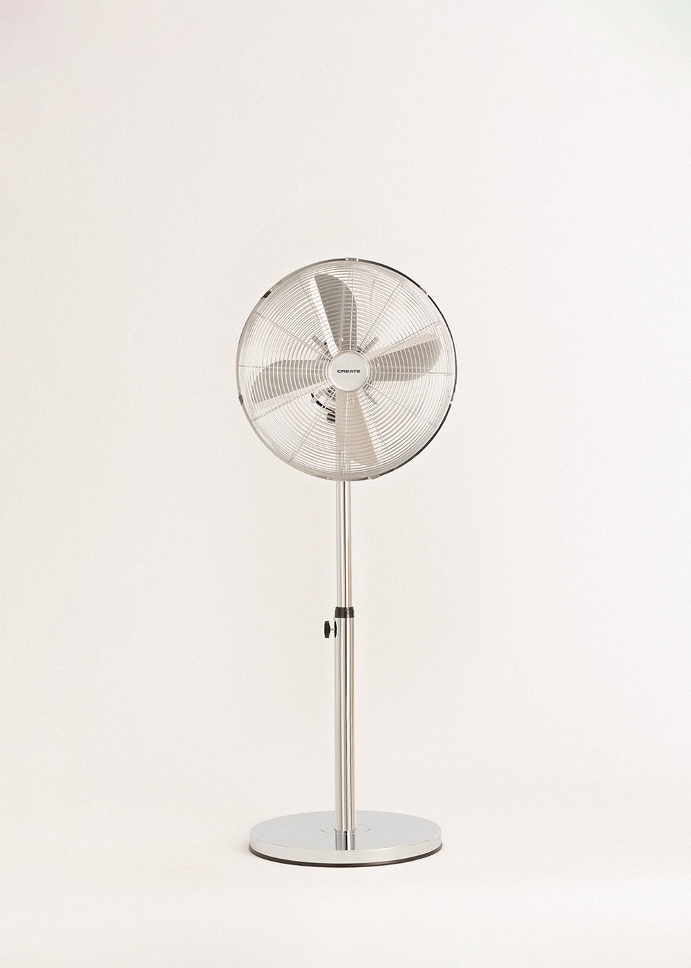 Un ventilador de pie plateado con cabezal y aspas redondos está centrado sobre un fondo blanco. La base también es plateada y redonda.