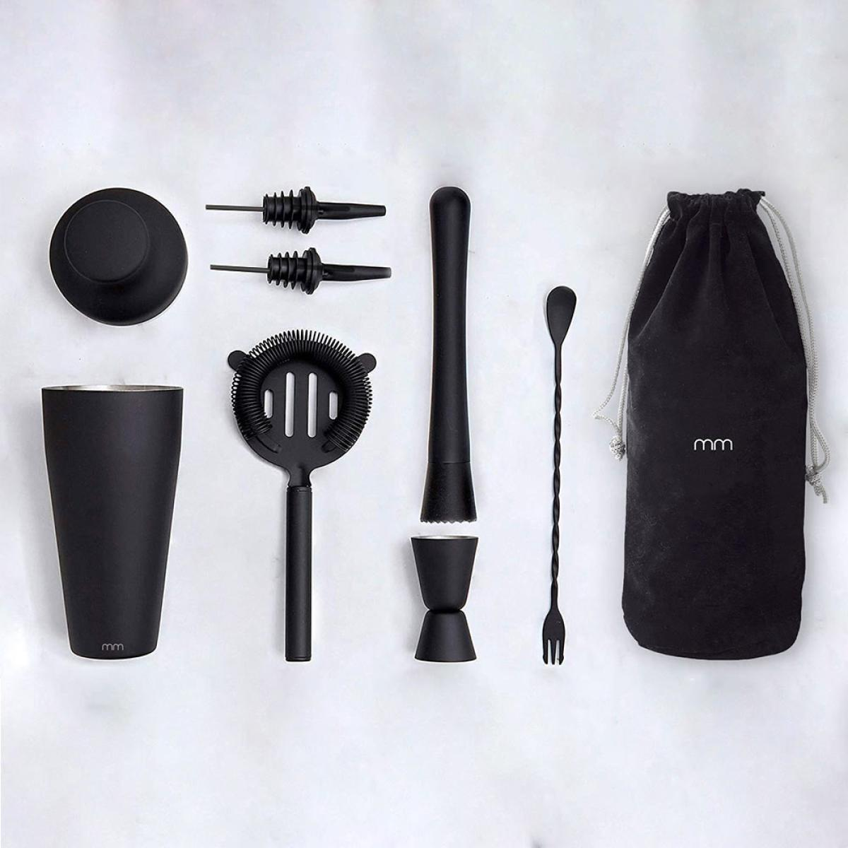 Black cocktail set with shaker, strainer, muddler, jigger, spoon, fork, pourers, and bag, arranged on a white surface.