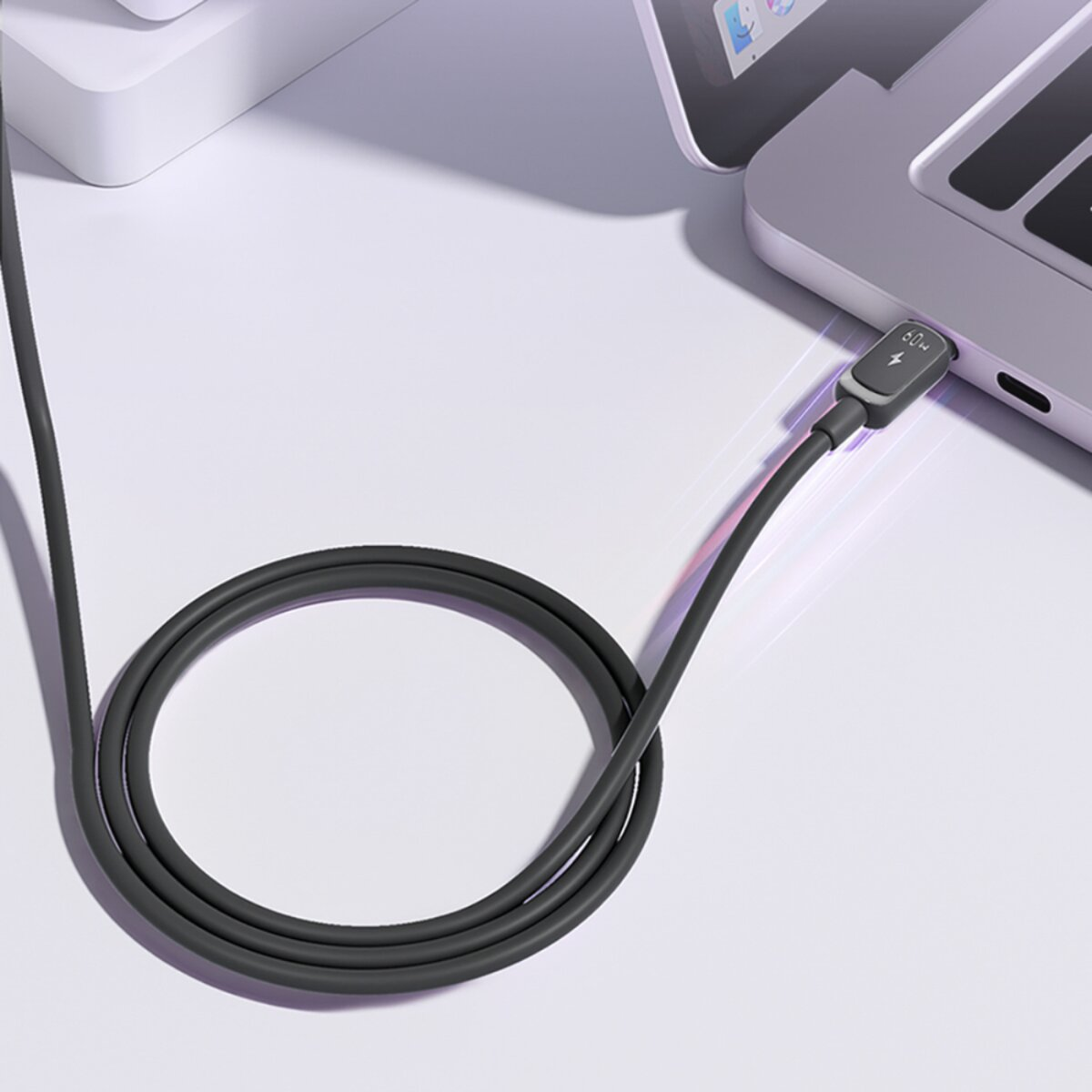 Un câble de chargement gris est branché sur un ordinateur portable. Le câble forme une boucle sur la surface blanche. Le chargeur affiche 60W.