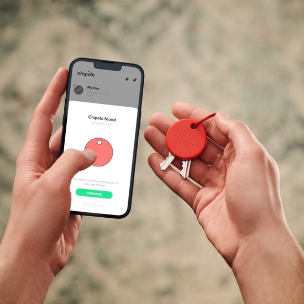 A person holds a phone and keys. The phone shows a Chipolo app. A red Chipolo tag is attached to the keys.