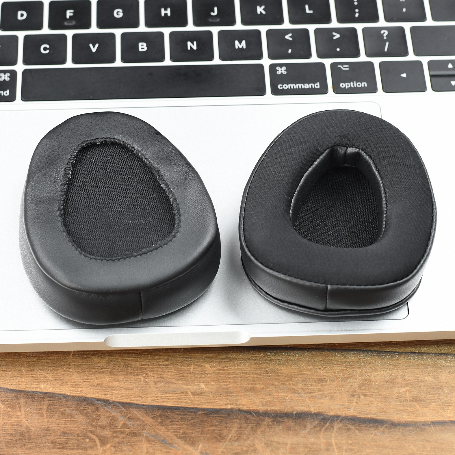 Due cuscinetti auricolari neri per cuffie su una tastiera di un laptop. La tastiera è bianca e la superficie è in legno.