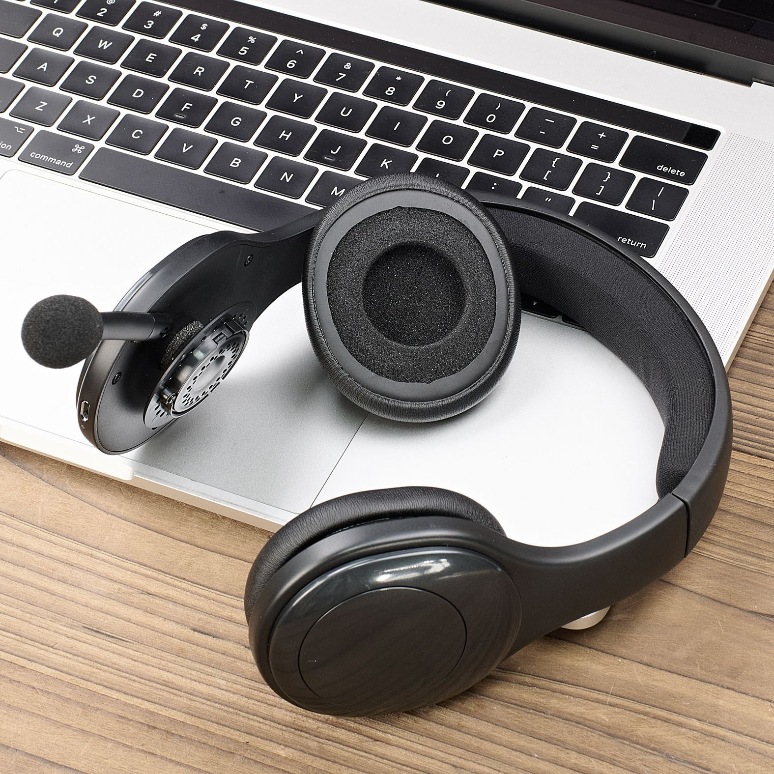 Cuffie nere con microfono su tastiera di laptop aperto, su superficie di legno.