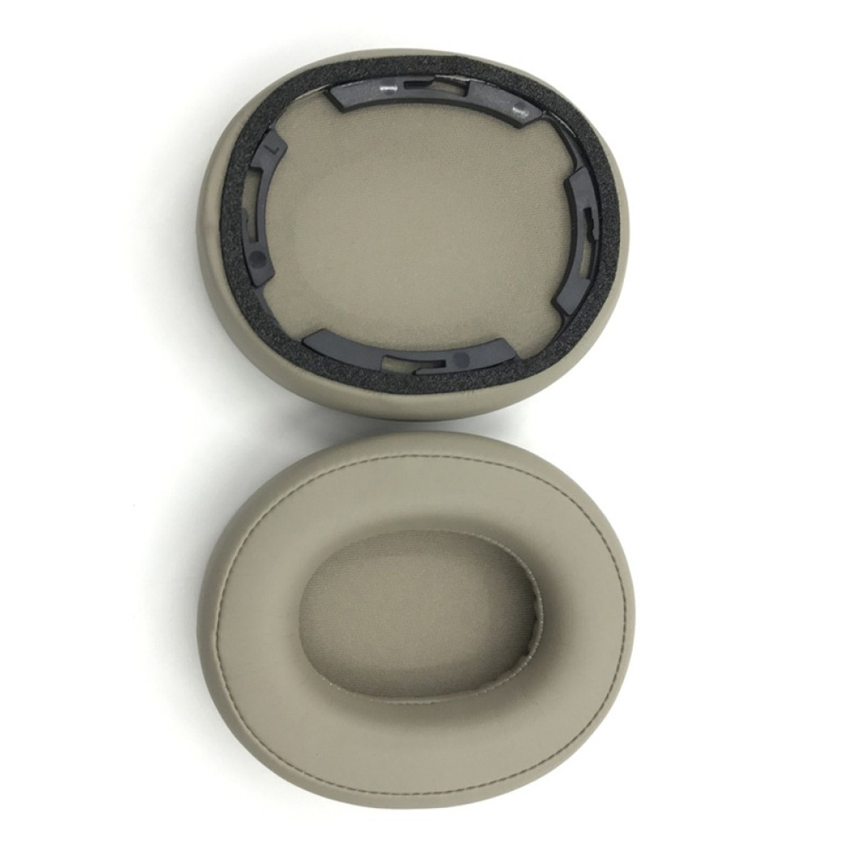 Due cuscinetti auricolari beige per cuffie. Uno ha un telaio interno nero. Entrambi poggiano su una superficie bianca.