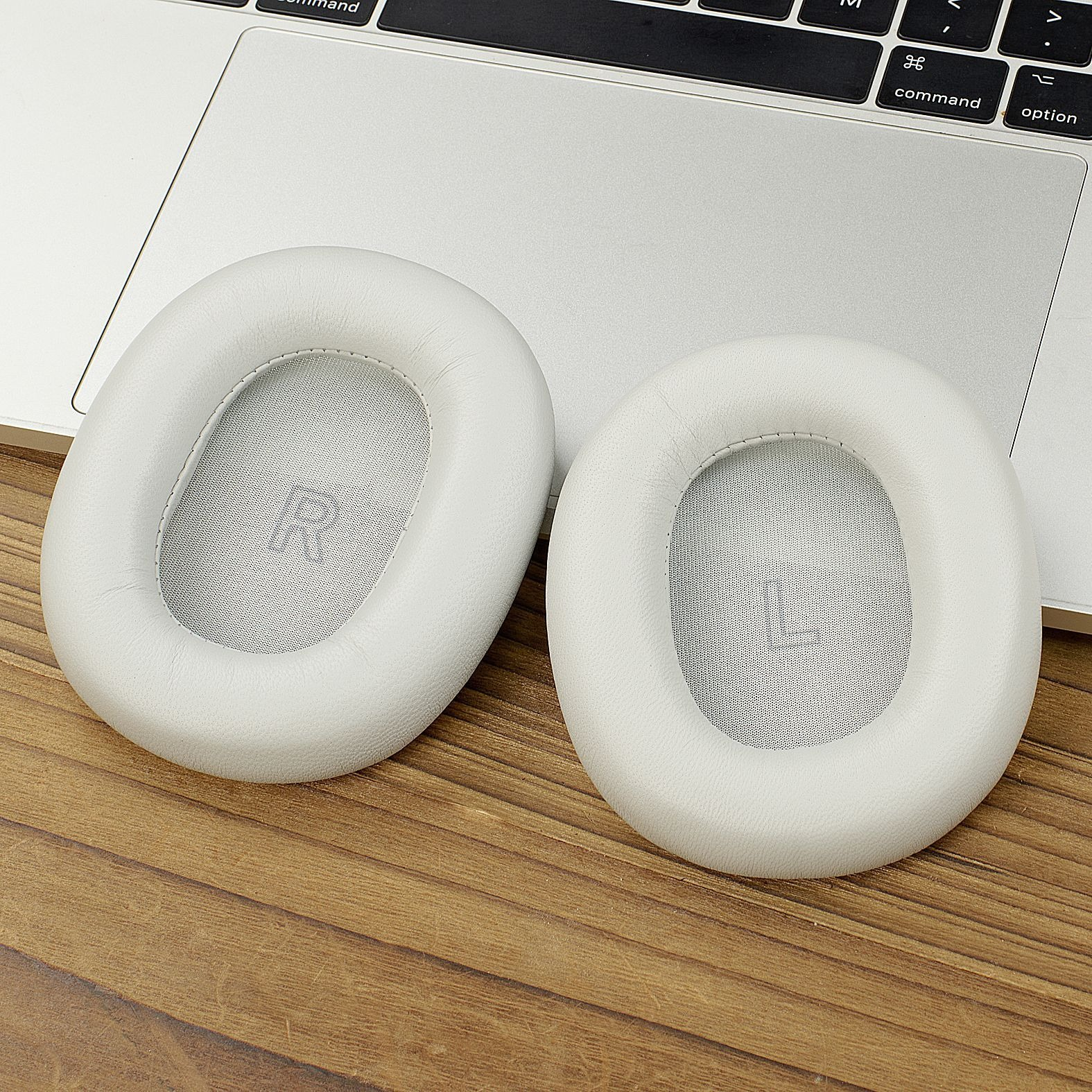 Due cuscinetti bianchi per cuffie su una tastiera di un laptop e su una superficie in legno. Uno ha una 'R', l'altro una 'L'.
