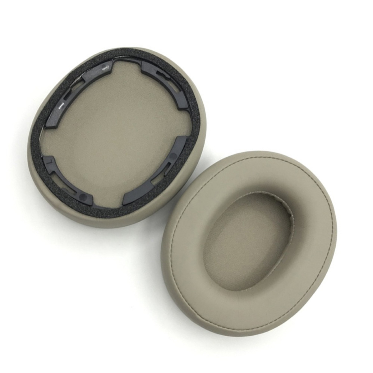Due cuscinetti auricolari beige per cuffie su sfondo bianco. Un cuscinetto è smontato, mostrando parti in plastica nera. Entrambi sono di forma ovale.