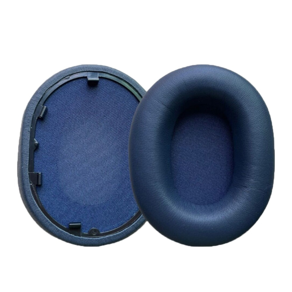 Due cuscinetti auricolari blu navy per cuffie. Uno è staccato, mostrando l'interno in tessuto. L'altro è intatto.
