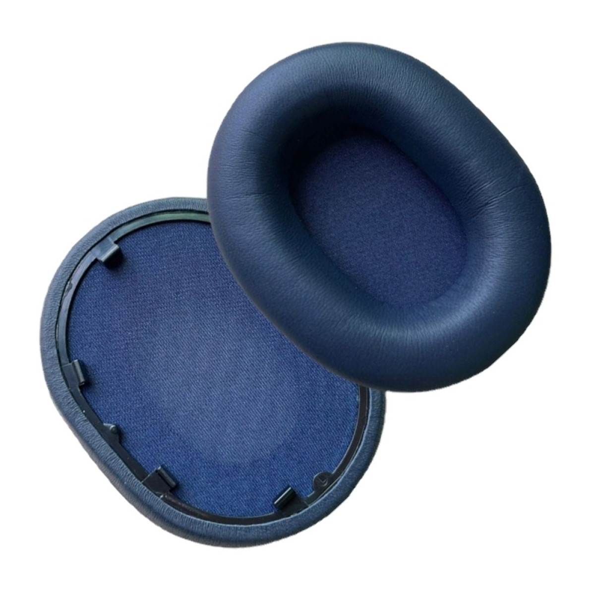 Due cuscinetti blu per cuffie, uno staccato. I cuscinetti sono ovali, con morbida pelle e tessuto, su sfondo bianco.