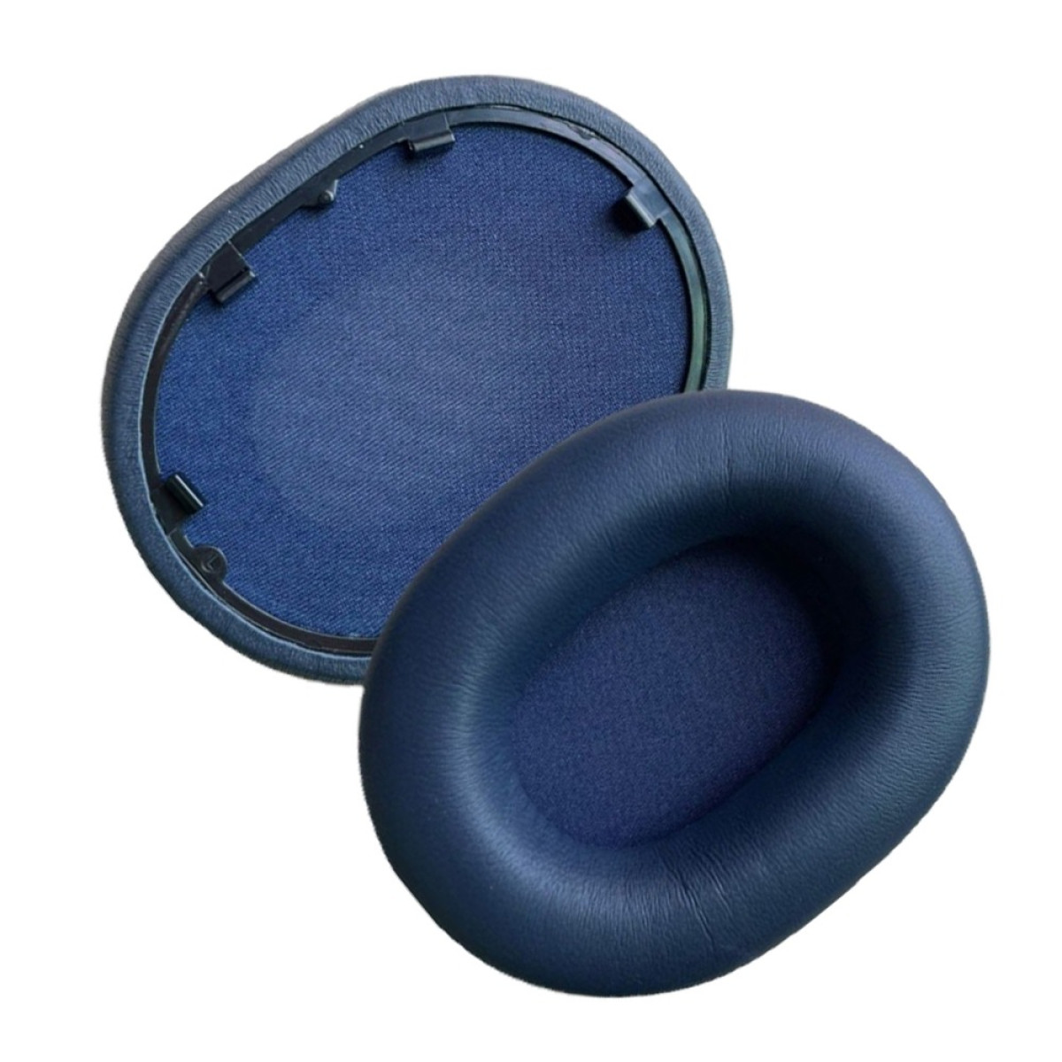 Due cuscinetti auricolari blu navy. Uno è staccato, mostrando l'interno in rete. L'altro è intero.