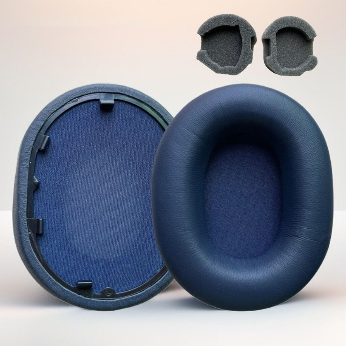 Cuffie e cuscinetti in schiuma. Cuffie blu scuro con tessuto blu scuro e due piccoli cuscinetti in schiuma grigia. Sfondo bianco.