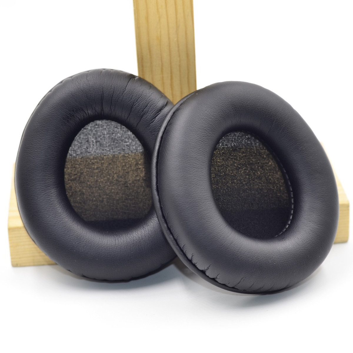 Due cuscinetti neri per cuffie davanti a una struttura in legno. I cuscinetti hanno un design rotondo e morbido.