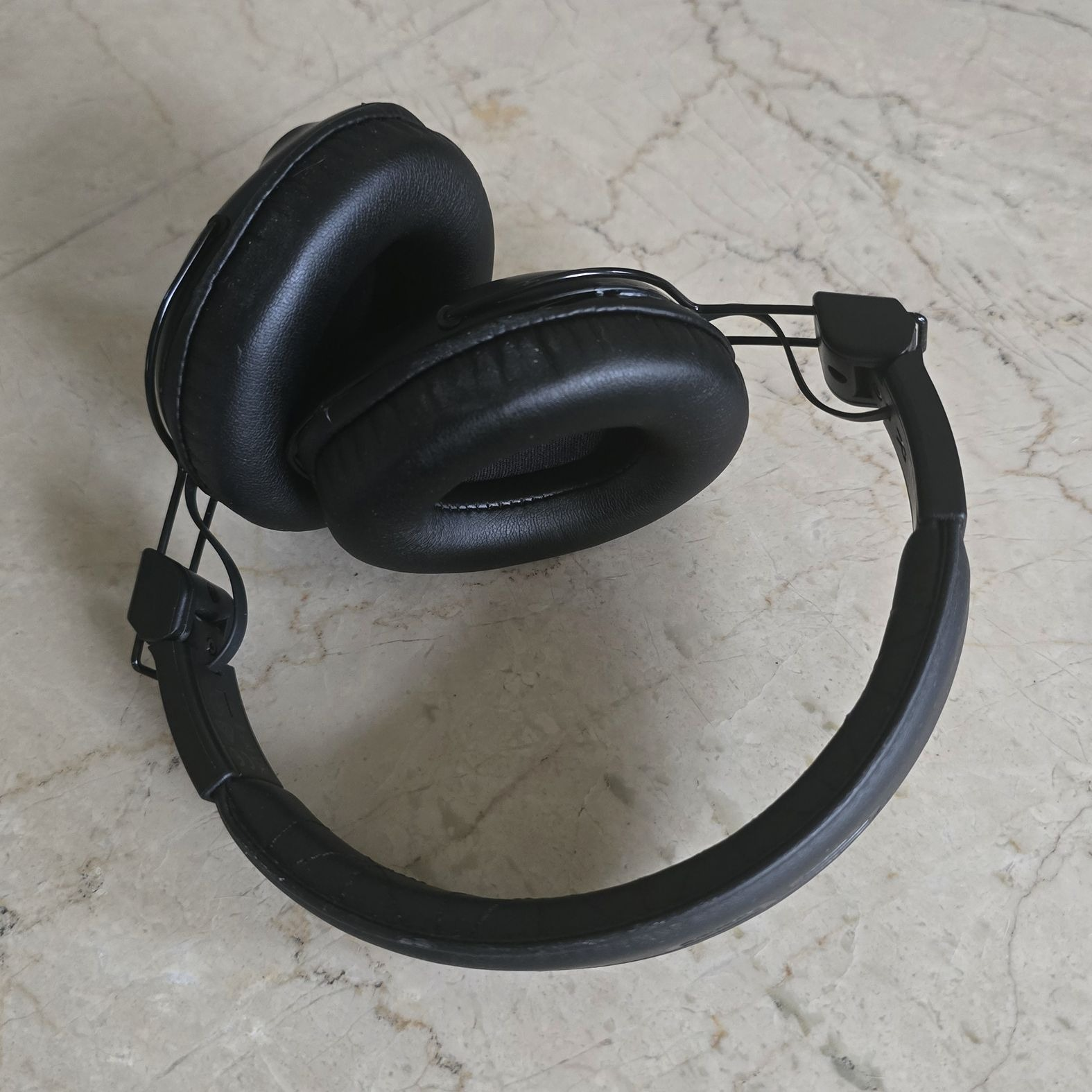 Cuffie nere su superficie marmorea. Le cuffie sono piegate, mostrando i padiglioni.