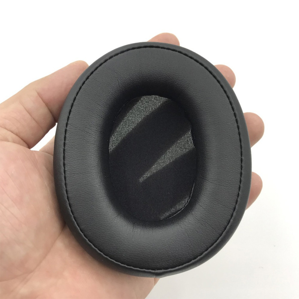 Un cuscinetto nero per cuffie è tenuto in mano su sfondo bianco. Il cuscinetto è di forma ovale con un centro a rete.