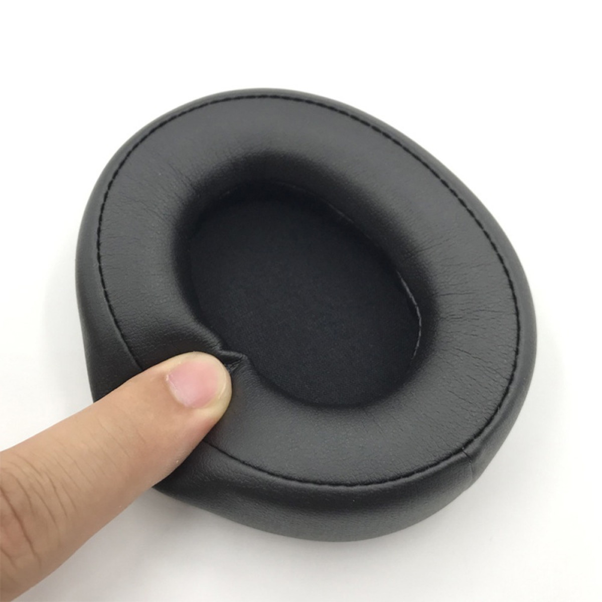 Un cuscinetto nero per le orecchie è tenuto da un dito su sfondo bianco. Il cuscinetto è di forma ovale, con superficie liscia.