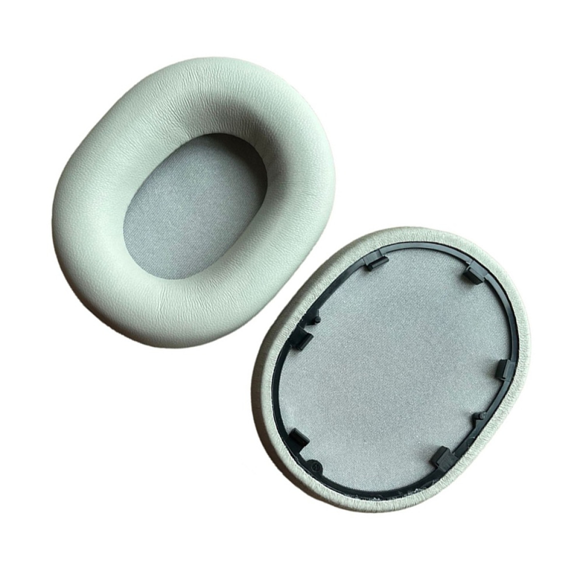 Due cuscinetti auricolari ovali grigi, uno con superficie morbida e l'altro con cornice in plastica nera e interno in rete, su sfondo bianco.