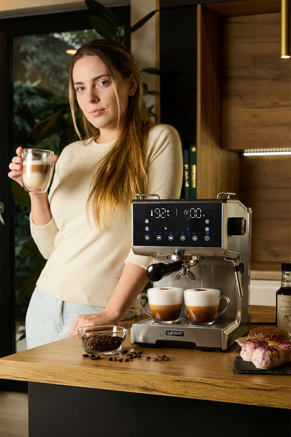 Kobieta trzyma kawę. Ekspres do kawy w tle. Filiżanki kawy, ziarna i ciasta na drewnianym blacie.