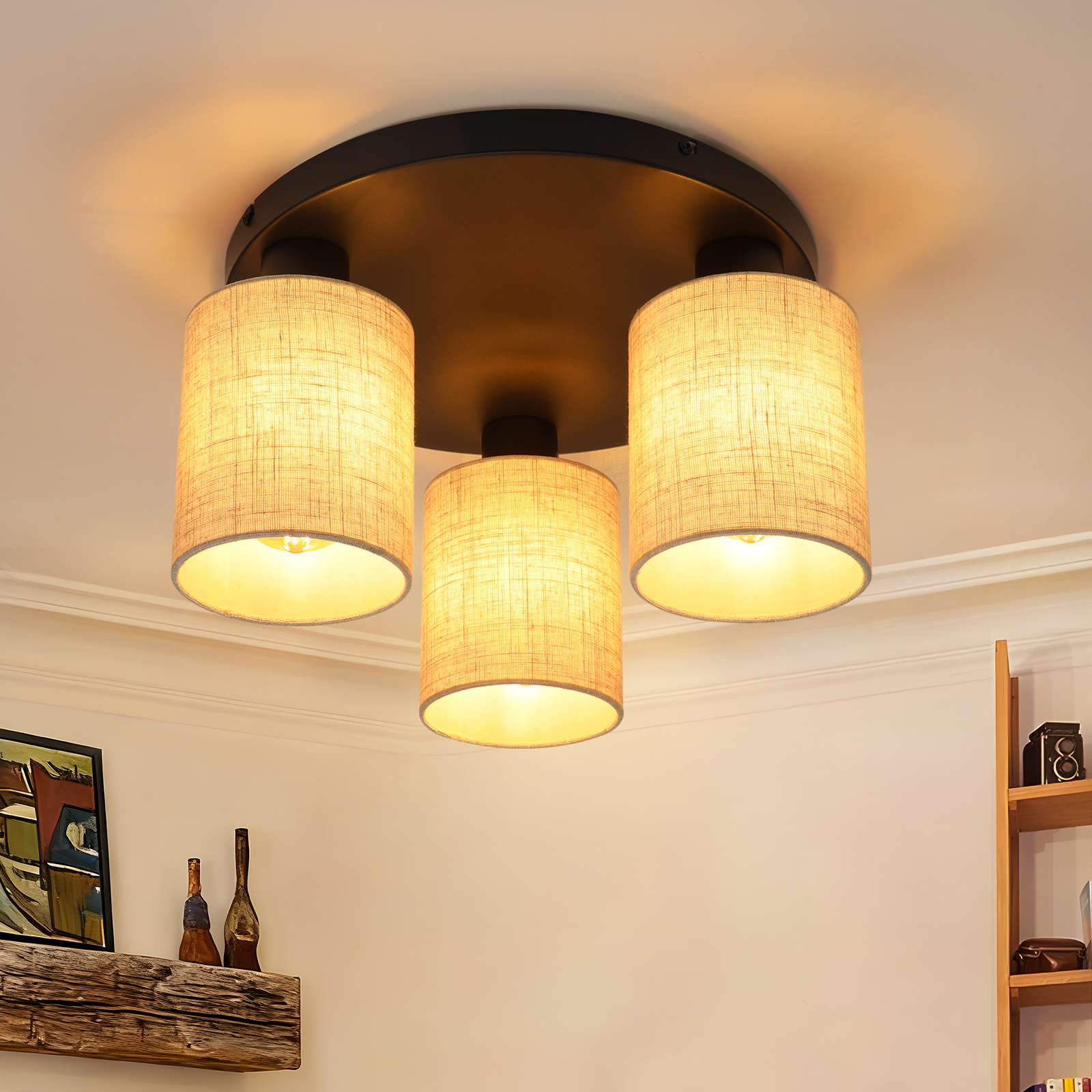 Lampa sufitowa z trzema cylindrycznymi kloszami. W tle widoczna drewniana półka i sztuka ścienna.