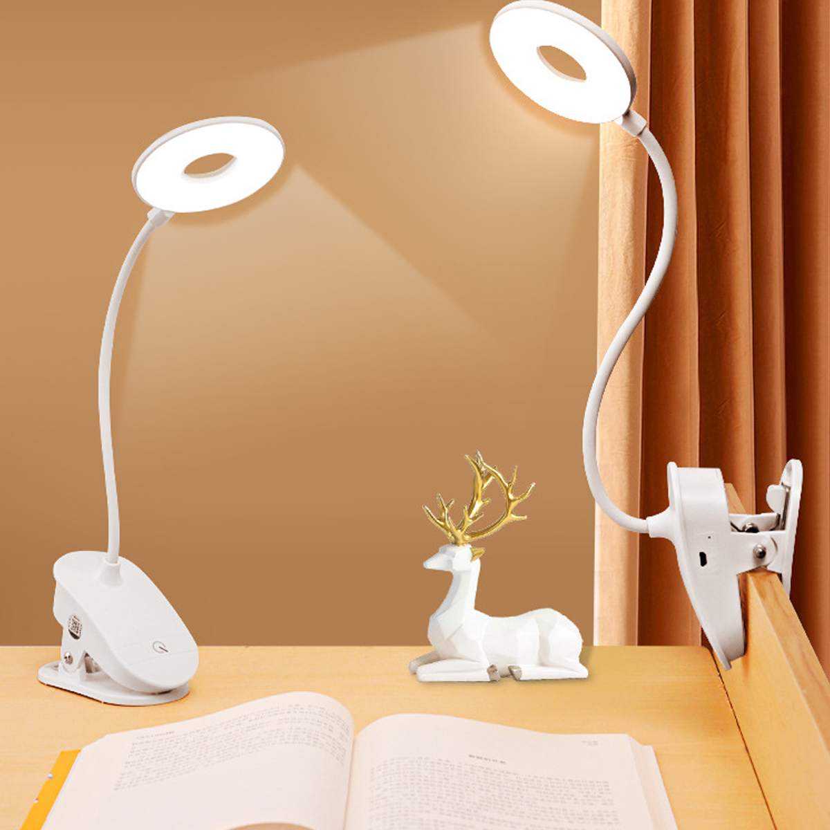 Zwei weiße Schreibtischlampen mit Ringlichtern. Auf dem Schreibtisch steht eine weiße Hirschstatue mit goldenem Geweih. Ein offenes Buch liegt im Vordergrund.