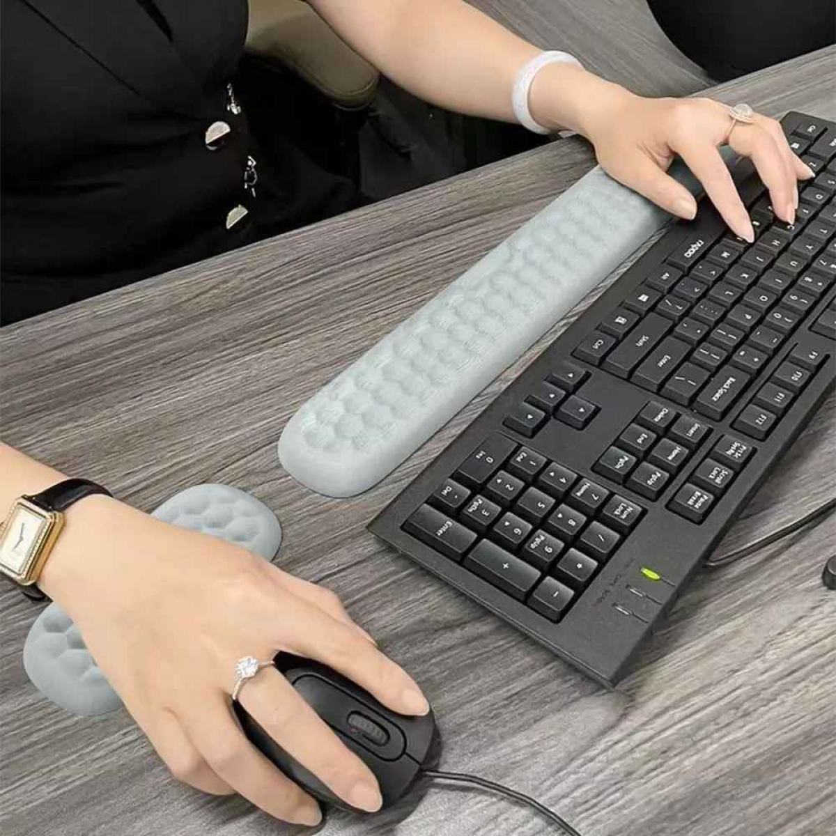 Eine Person benutzt einen Computer. Die Hände sind auf einer Tastatur und einer Maus. Es gibt eine Handgelenkauflage und ein Mauspad.