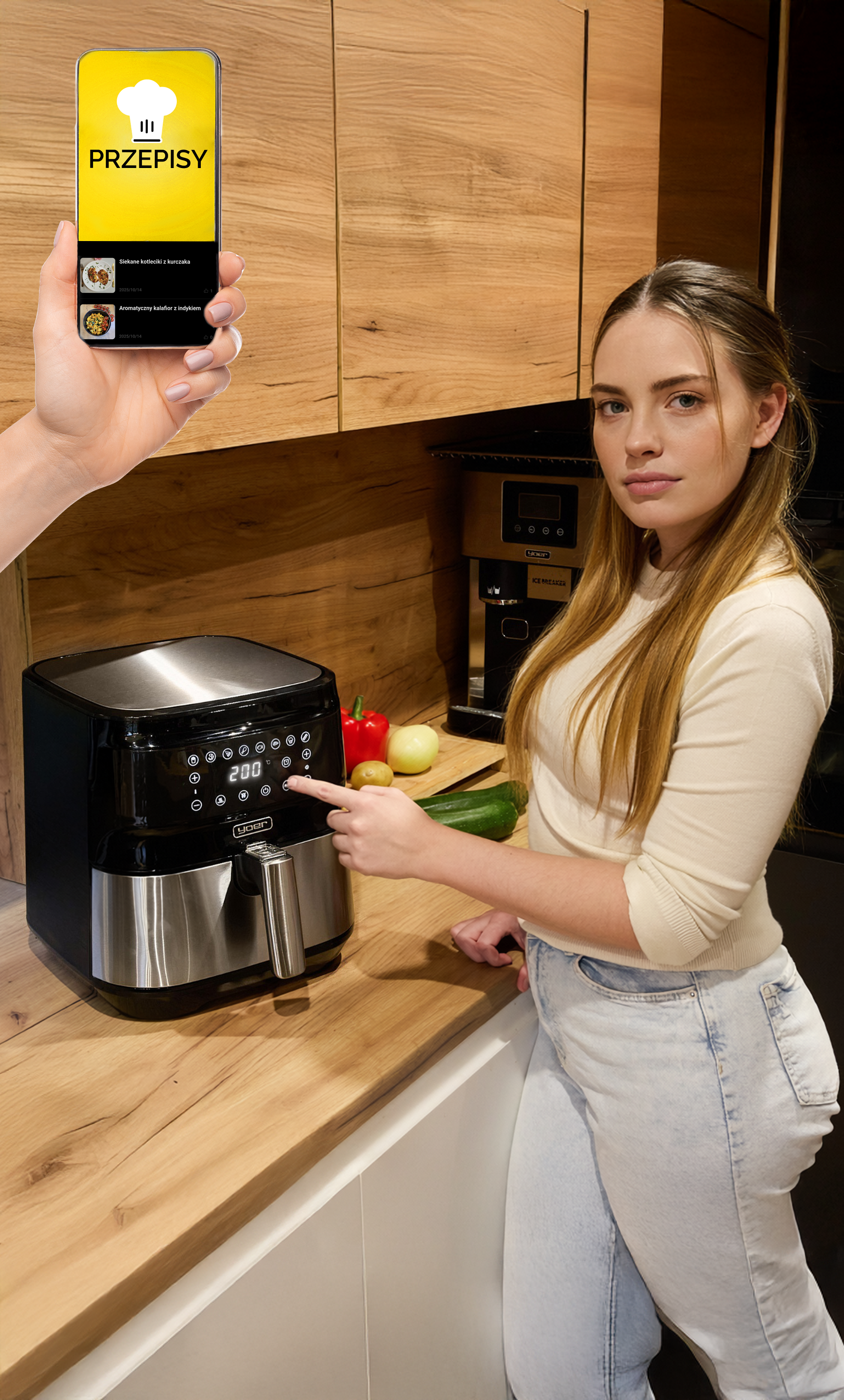 Kobieta w kuchni, frytkownica beztłuszczowa, telefon z przepisami. Dotyka frytkownicy. Warzywa na blacie.