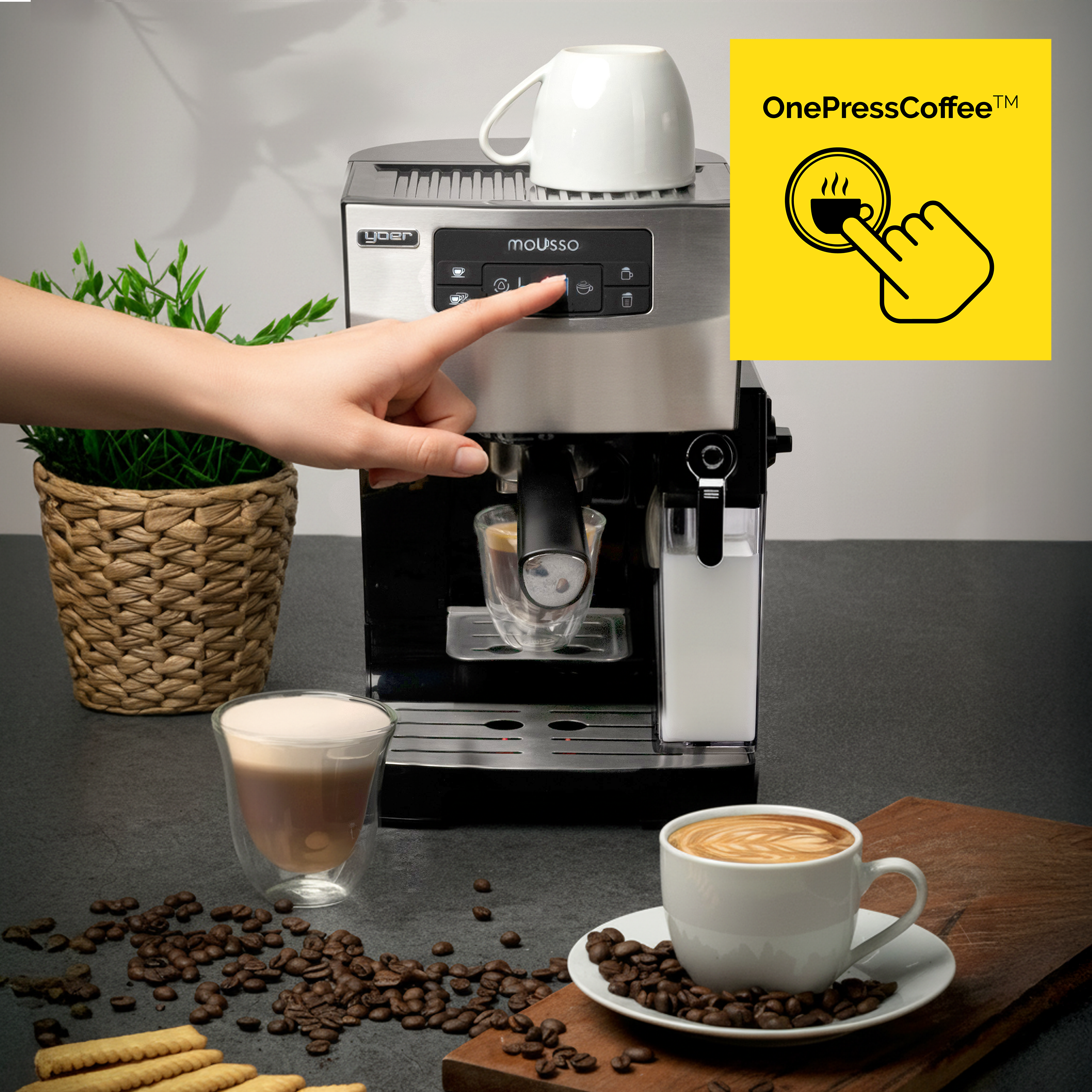 Ręka naciska przycisk na ekspresie do kawy. W scenie filiżanki, ziarna i rośliny.