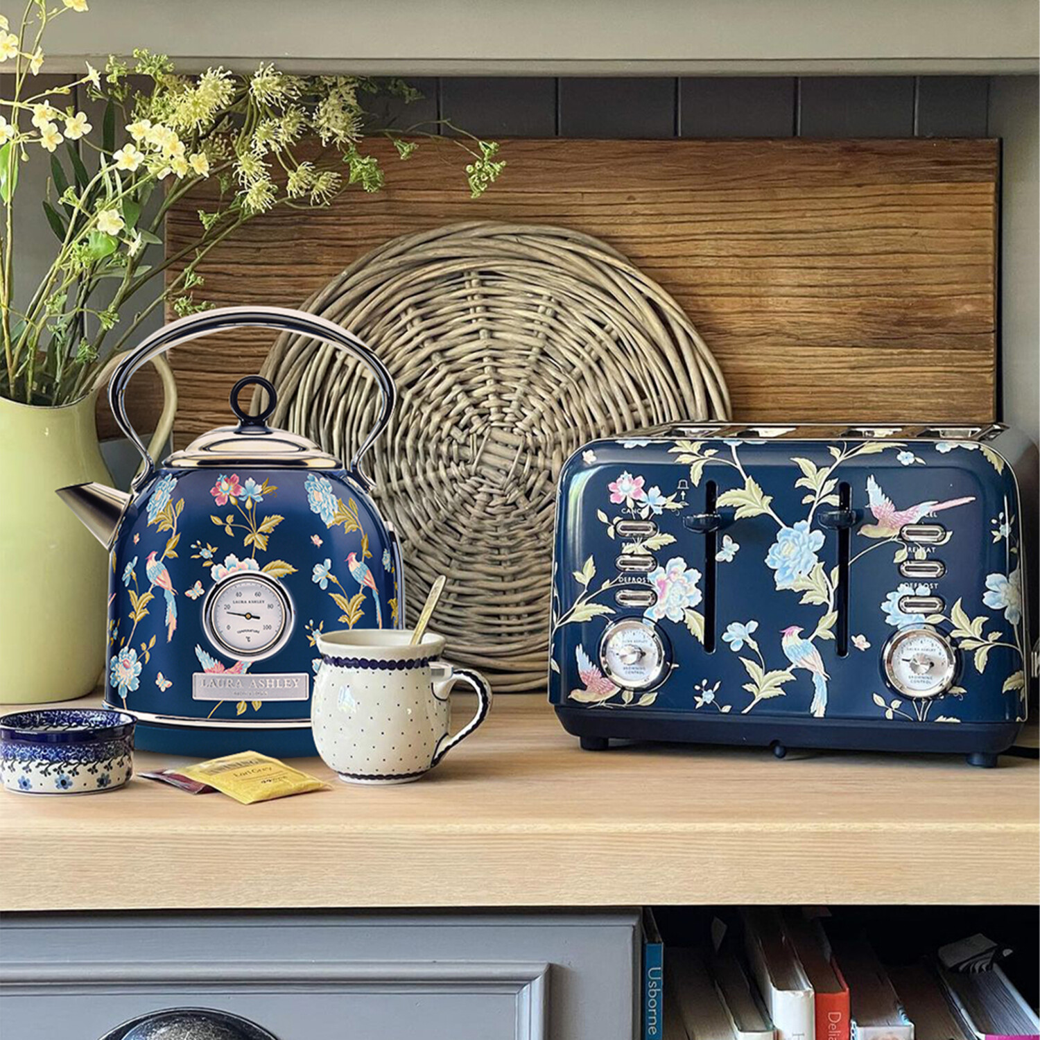 Ein marineblauer, floraler Wasserkocher und Toaster stehen auf einem Holzregal. Eine Tasse, eine Schüssel und Blumen sind in der Nähe.