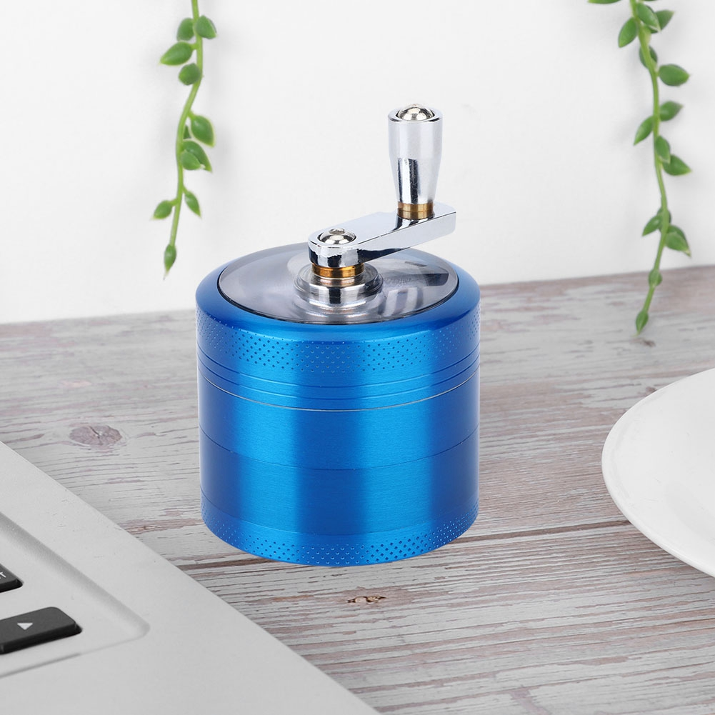 Ein blauer Grinder mit silbernem Griff steht auf einer Holzoberfläche neben einem Laptop und einem weißen Teller.