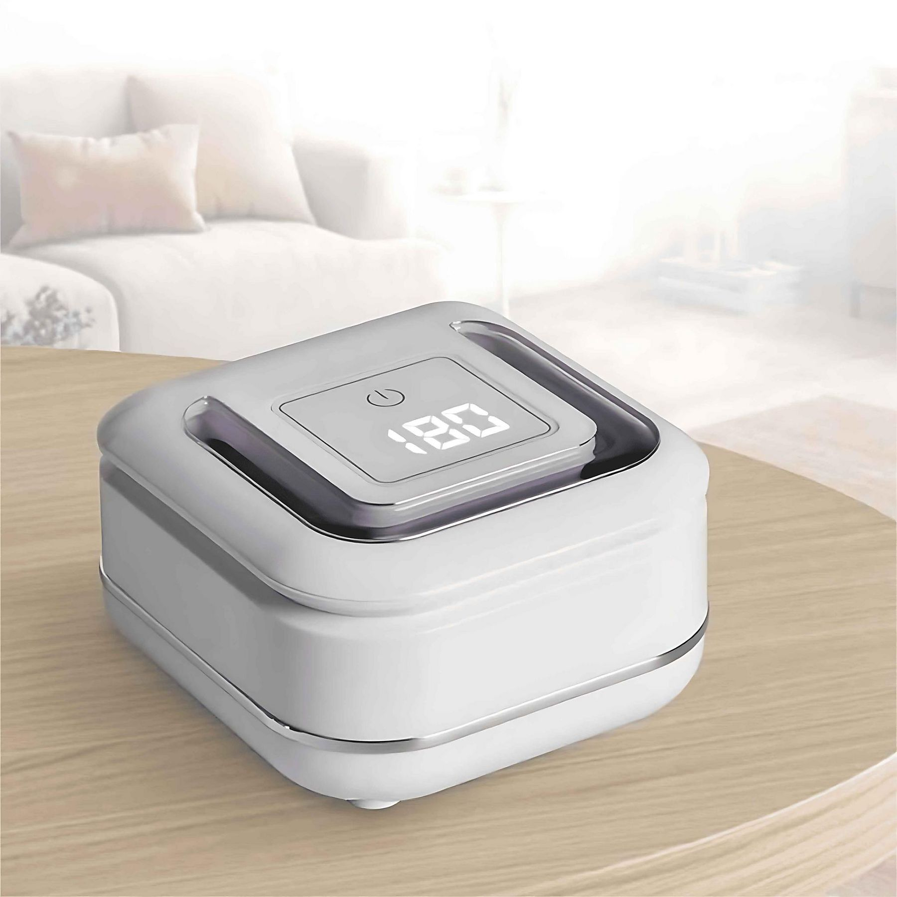 Weißes elektronisches Gerät auf einem Holztisch mit Digitalanzeige. Im Hintergrund eine verschwommene Couch.
