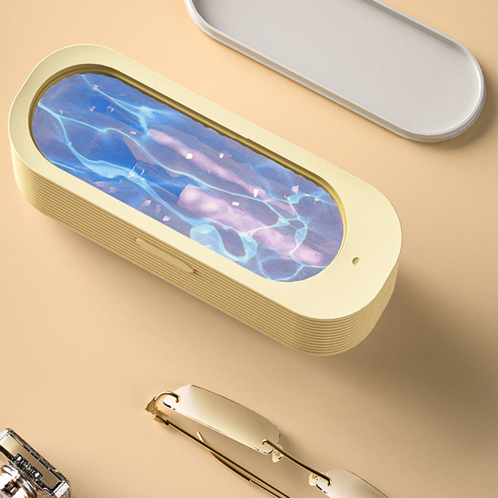 Eine gelbe rechteckige Box mit blauem und violettem Wassermuster, ein Tablett und eine Brille auf beigem Untergrund.